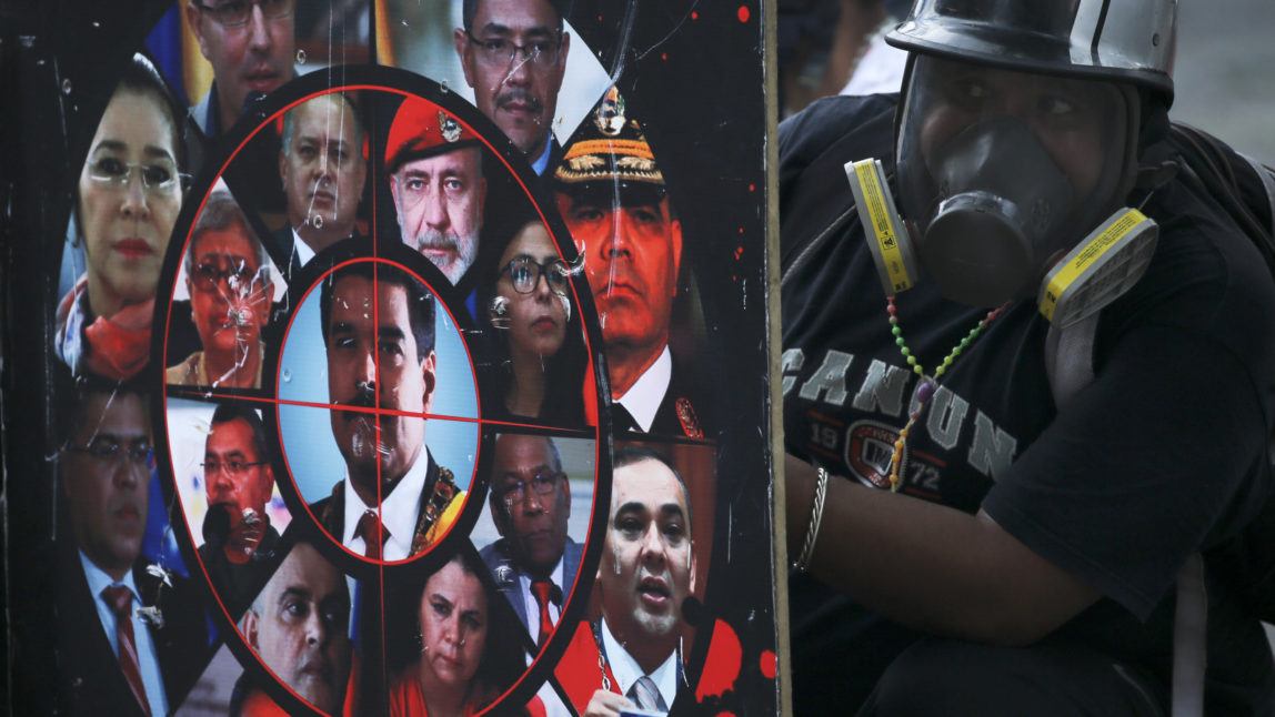 An anti-government protester holds a shield brandished with photos of President Nicolas Maduro, government officials and a gun sight, during clashes with security forces in Caracas, Venezuela, July 22, 2017. Fernando Llano | AP