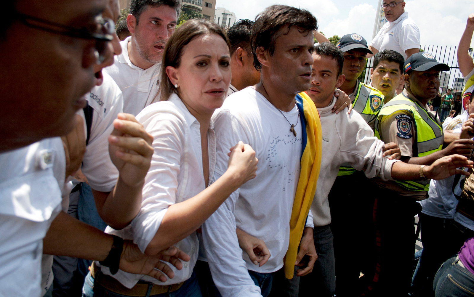 在2014年2月18日的照片中，委内瑞拉女议员Maria Corina Machado，左，和Leopoldo Lopez，中心，在洛佩兹向委内瑞拉加拉加斯的国民警卫投降之前，被反政府示威者包围。对于许多委内瑞拉人来说，反对党的两位最高层领导人，前总统候选人恩里克·卡普里莱斯和被判入狱的莱奥波尔多·洛佩兹，仍被视为脱离工人阶级生活的精英的一部分。 （美联社/ Juan Manuel Hernandez）