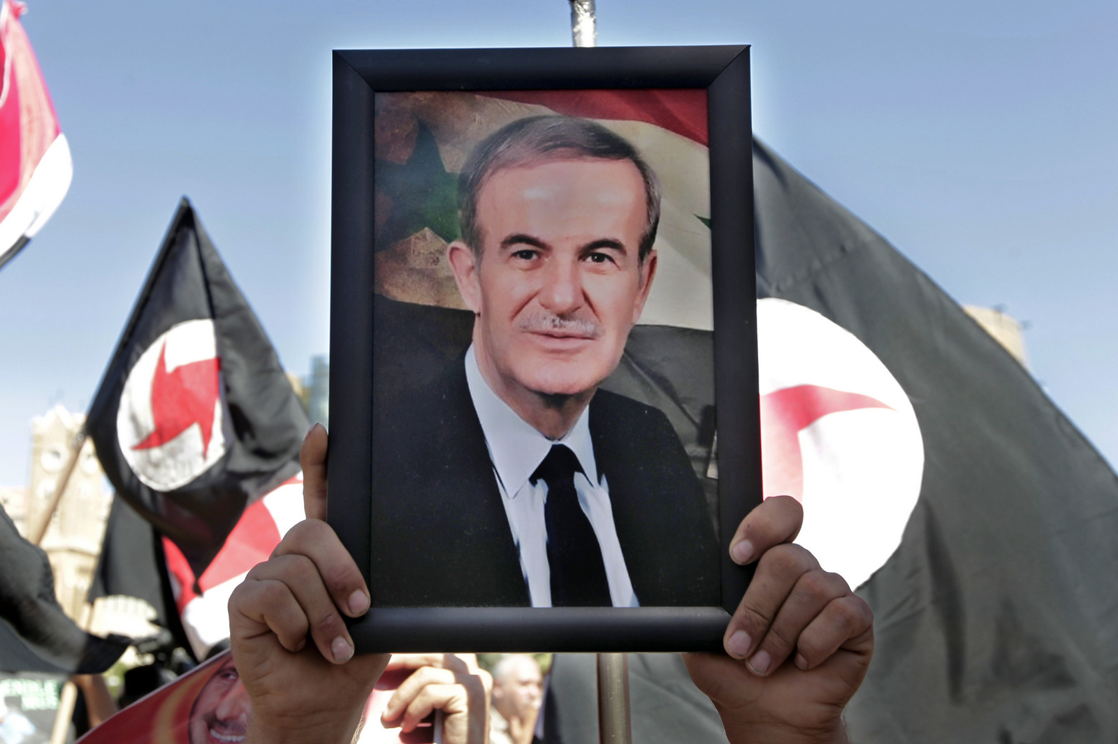 The Syrian Social Nationalist Party logo is seen behind a portrait of late Syrian President Hafez Assad during a demonstration against possible US military action in Syria, in front of the UN headquarters, in Beirut, Lebanon,, Sept. 8, 2013. (AP/Bilal Hussein)