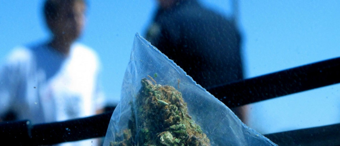 A small bag of marijuana is shown in the foreground as a man talks to Idaho State Police Trooper Justin Klitch in Fruitland, Idaho in the background. (AP/Nigel Duara)