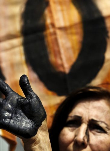 An activist with her hand painted black to symbolize the contamination of oil, takes part in a protest performance demanding measures to prevent oil spills, outside the national oil company in Lima, Peru, Aug. 22, 2016. (AP/Rodrigo Abd)