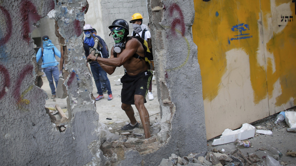 A masked anti-government demonstrator breaks down a wall to release pieces of concrete to throw at police during a protest against the installation of a constitutional assembly in Caracas, Venezuela, Aug. 4, 2017. (AP/Ariana Cubillos)