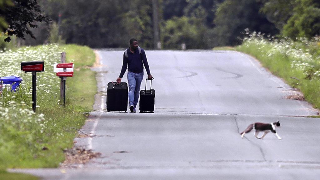 Dulne Brutus, of Haiti, tows his luggage down Roxham Road in Champlain, N.Y., while heading to an unofficial border station across from Saint-Bernard-de-Lacolle, Quebec, Aug. 7, 2017. Officials on both sides of the border first began to notice last fall, around the time of the U.S. presidential election, that more people were crossing at Roxham Road. Since then the numbers have continued to climb. (AP/Charles Krupa)