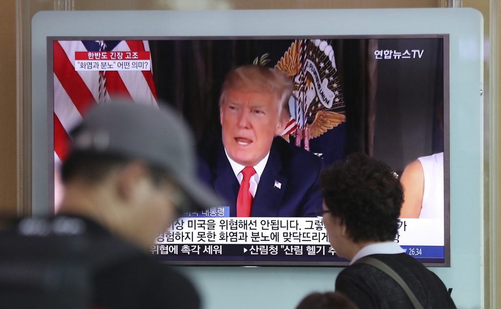 People walk by a TV screen showing a local news program reporting with an image of U.S. President Donald Trump at the Seoul Train Station in Seoul, South Korea, Aug. 9, 2017. (AP/Lee Jin-man)
