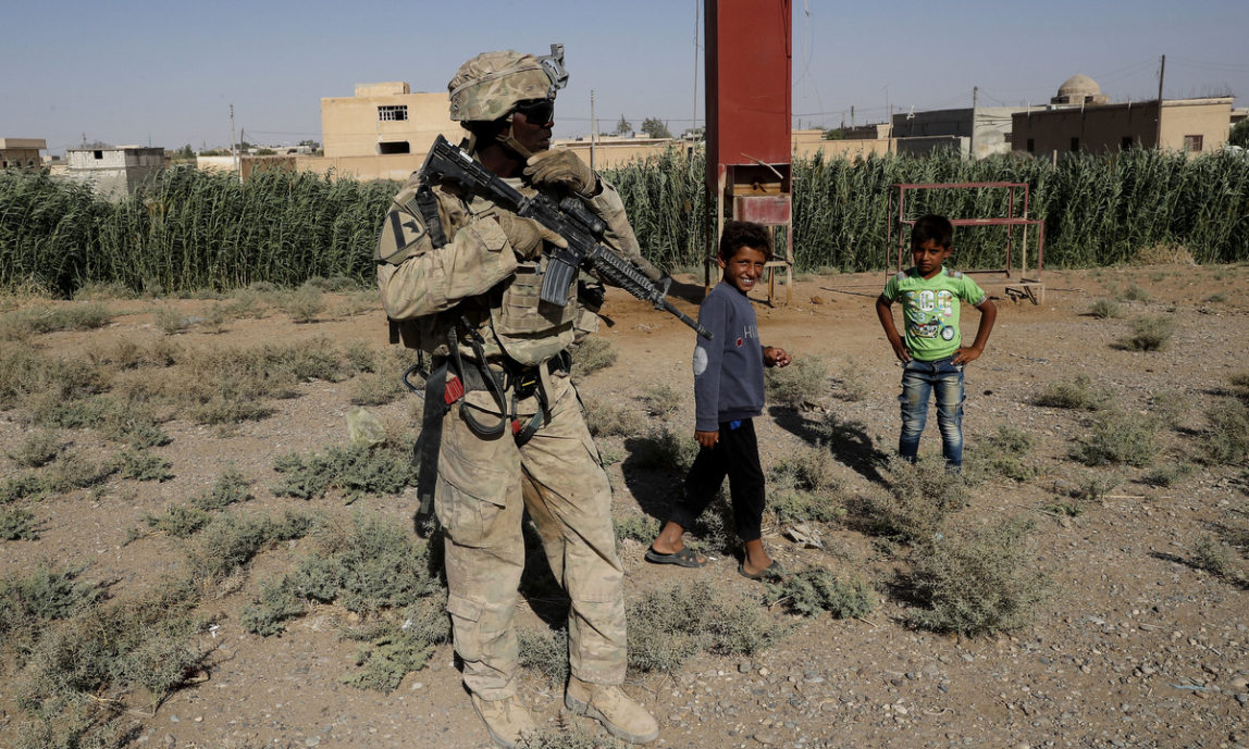 A U.S. soldier stands near Syrian children on a road that links to Raqqa, Syria, Wednesday, July 26, 2017.(AP/Hussein Malla)