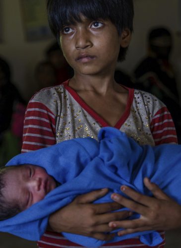 Rohingya Muslim girl Afeefa Bebi, who recently crossed over from Myanmar into Bangladesh, holds her few-hours-old brother as doctors check her mother Yasmeen Ara at a community hospital in Kutupalong refugee camp, Bangladesh, Wednesday, Sept. 13, 2017. The family crossed into Bangladesh on Sept. 3. Recent violence in Myanmar has driven hundreds of thousands of Rohingya Muslims to seek refuge across the border in Bangladesh. But Rohingya have been fleeing persecution in Buddhist-majority Myanmar for decades, and many who have made it to safety in other countries still face a precarious existence. (AP Photo/Dar Yasin)