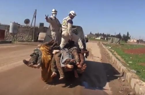 Screenshot from video showing White Helmets standing on top of Syrian Arab Army soldiers bodies, whose boots have been stolen or removed.