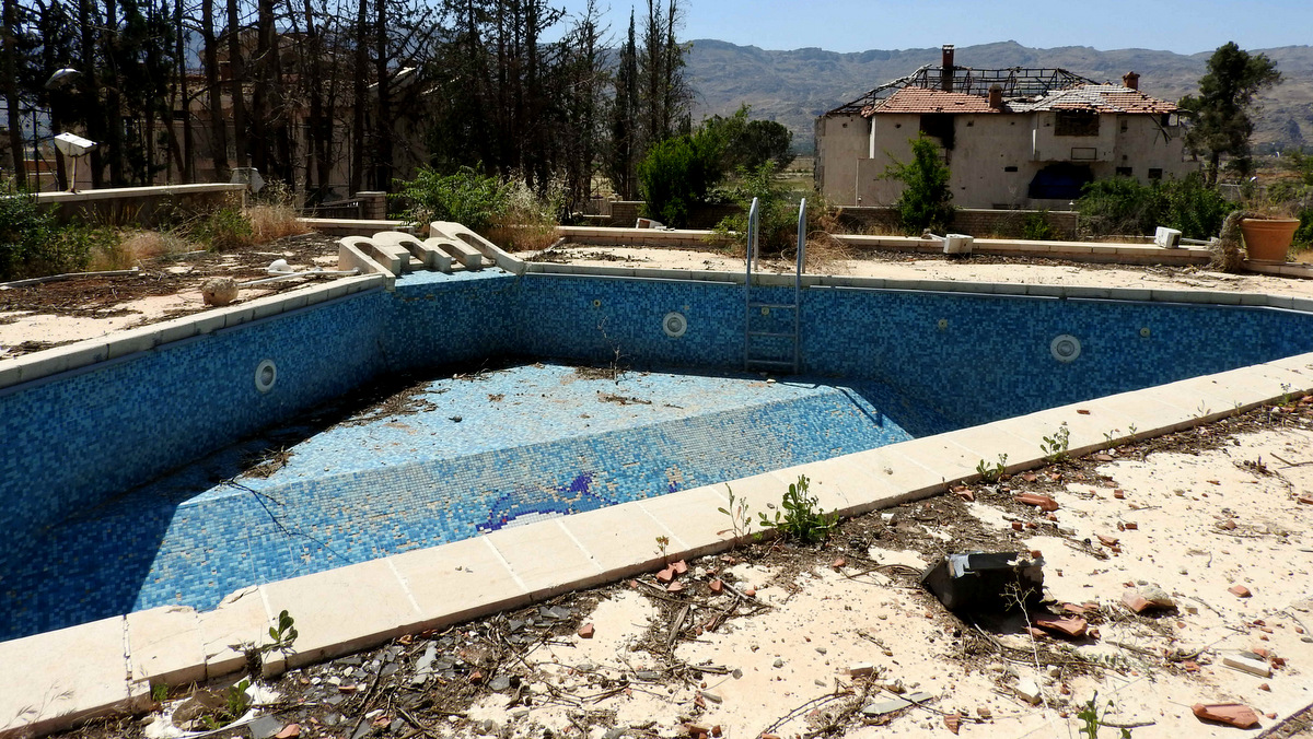 The outside of a villa used by rebels as a tunnel entrance. The idyllic mountain view was marred only by the signs of battle: an empty swimming pool lightly littered with rubble, and a villa beyond, roof and walls blown out by shelling. (Photo: Eva Bartlett/MintPress News)