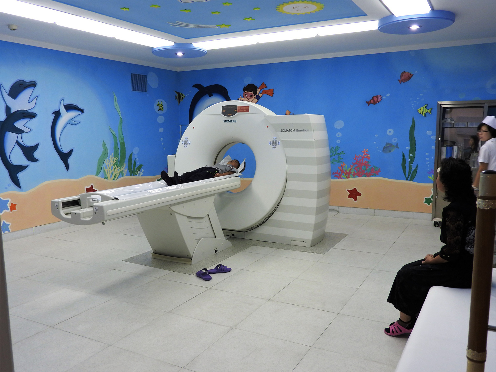 El Okryu Children's Hospital es una instalación de seis pisos y 300 camas frente al hospital de maternidad de Pyongyang. Las sanciones de EE. UU. En la RPDC impiden la entrada adicional de máquinas como la tomografía computarizada en la imagen. Aunque desafiadamente orgullosa del sistema de atención médica, la Dra. Kim Un-Song habló de su ira como madre: "Esto es inhumano y en contra de los derechos humanos. La medicina que necesitan los niños está bajo sanciones ".