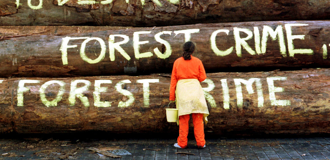 A Greenpeace campaigner writes "Forest Crime" and "G8 destroys forests" on logs at the port of Nordenham, northwest Germany, Thursday, July 20, 2000. (AP/Joerg Sarbach)