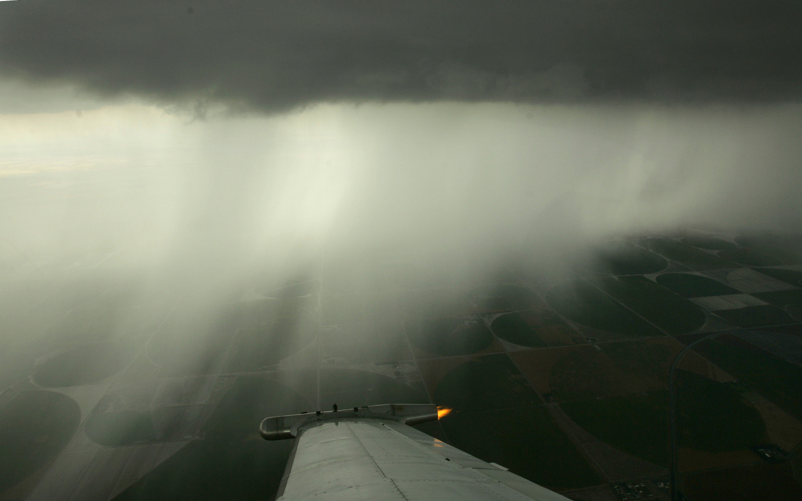 A wing-mounted generator emits particles of silver iodide as circular fields of crops are seen in the distance during a cloud seeding mission for the Western Kansas Weather Modification program Aug. 28, 2007, near Lakin, Kan. (AP/Charlie Riedel)