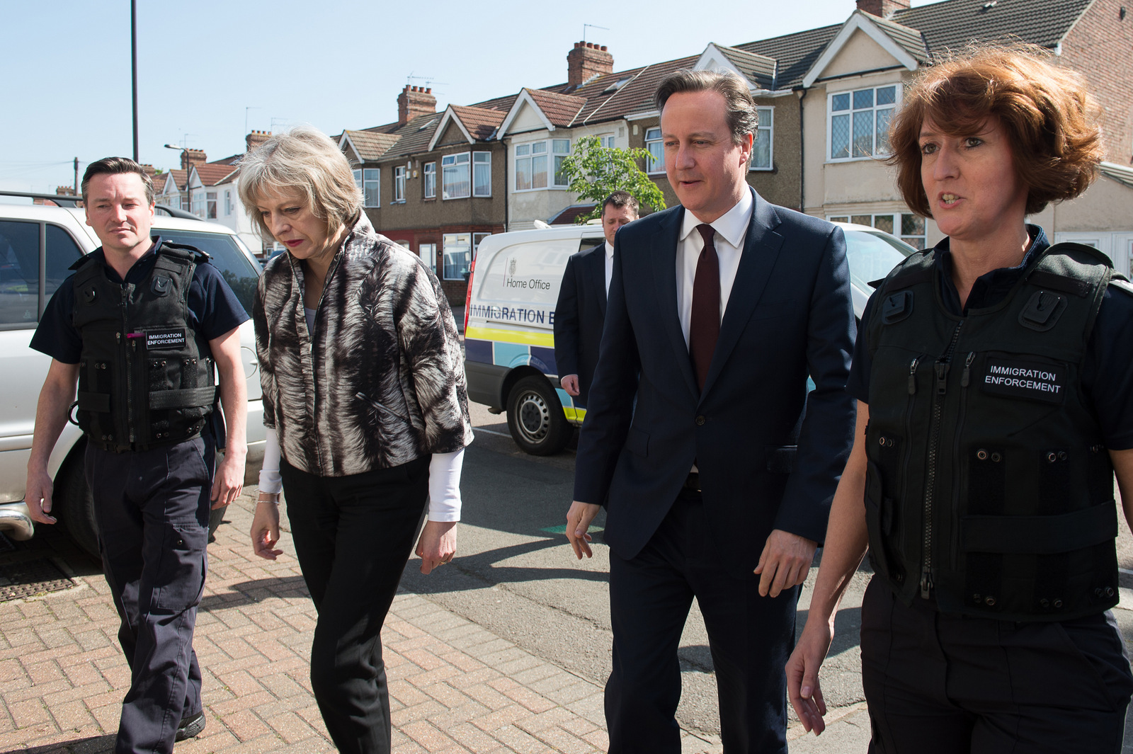 Britain's Prime Minister David Cameron and Home Secretary Theresa May talk to Immigration Enforcement officers after officers raided residential properties looking for illegal immigrants in Southall, London, Thursday May 21, 2015. Cameron on Thursday announced strict new measures designed to control immigration to Britain as new official figures show increasing levels of migration. (Laura Lean/Pool Photo via AP)