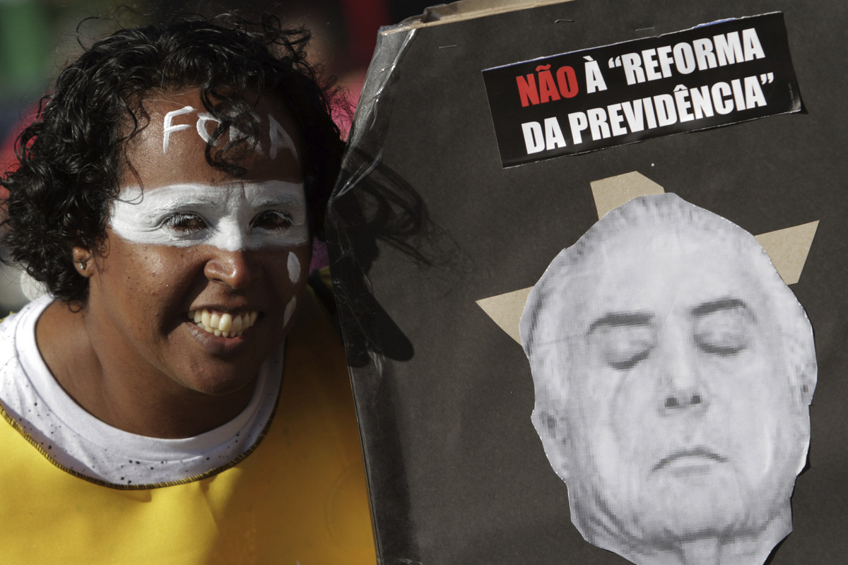 A woman, with the Portuguese word for "Out" painted on her forehead, poses next to a montage featuring Brazil's President Michel Temer and the message "No to welfare reform", during an anti-government protest in Brasilia, Brazil, May 24, 2017. (AP/Eraldo Peres)