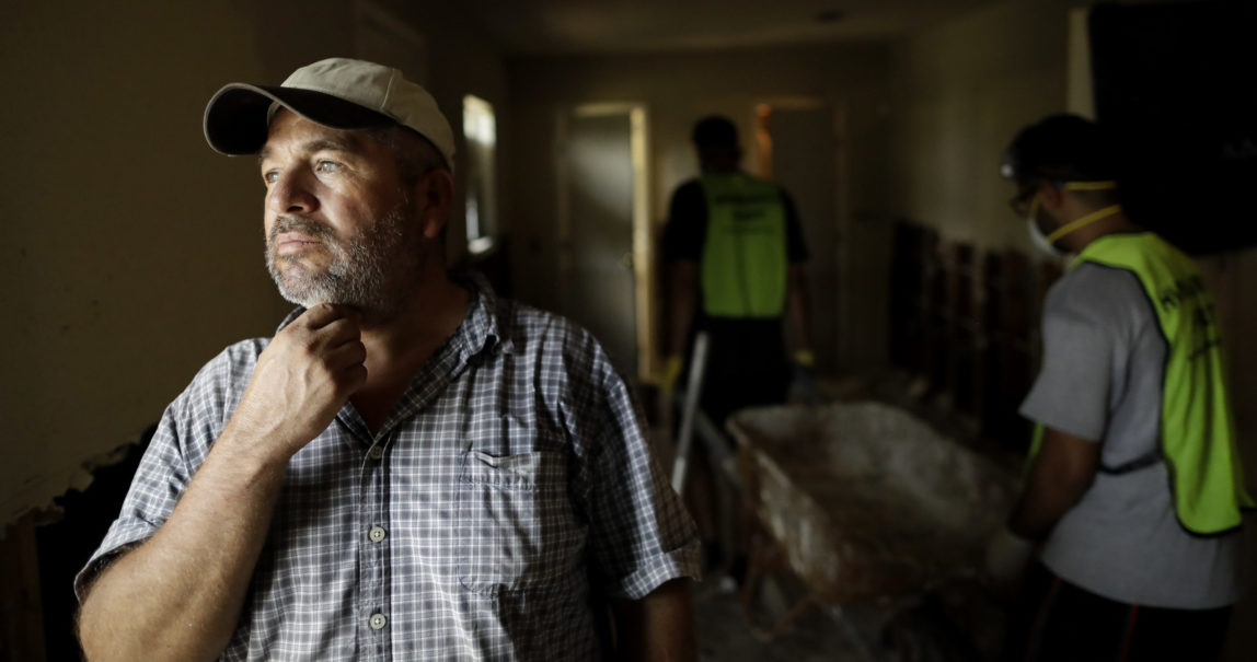 In this Sunday, Sept. 3, 2017, photo, Lino Saldana looks out his window towards the bayou that overflowed into his home as volunteers from the Ahmadiyya Muslim Youth Association help him clean out debris in Houston. Like many of his neighbors on flood-ravaged Minden Street, Saldana knows that if he doesn't work, he doesn't get paid. Harvey's epic 52 inches of rain didn't discriminate between rich and poor areas with its flooding, but in working-class neighborhoods where many live paycheck to paycheck, the cleanup and recovery could be an even tougher slog. (AP/Gregory Bull)