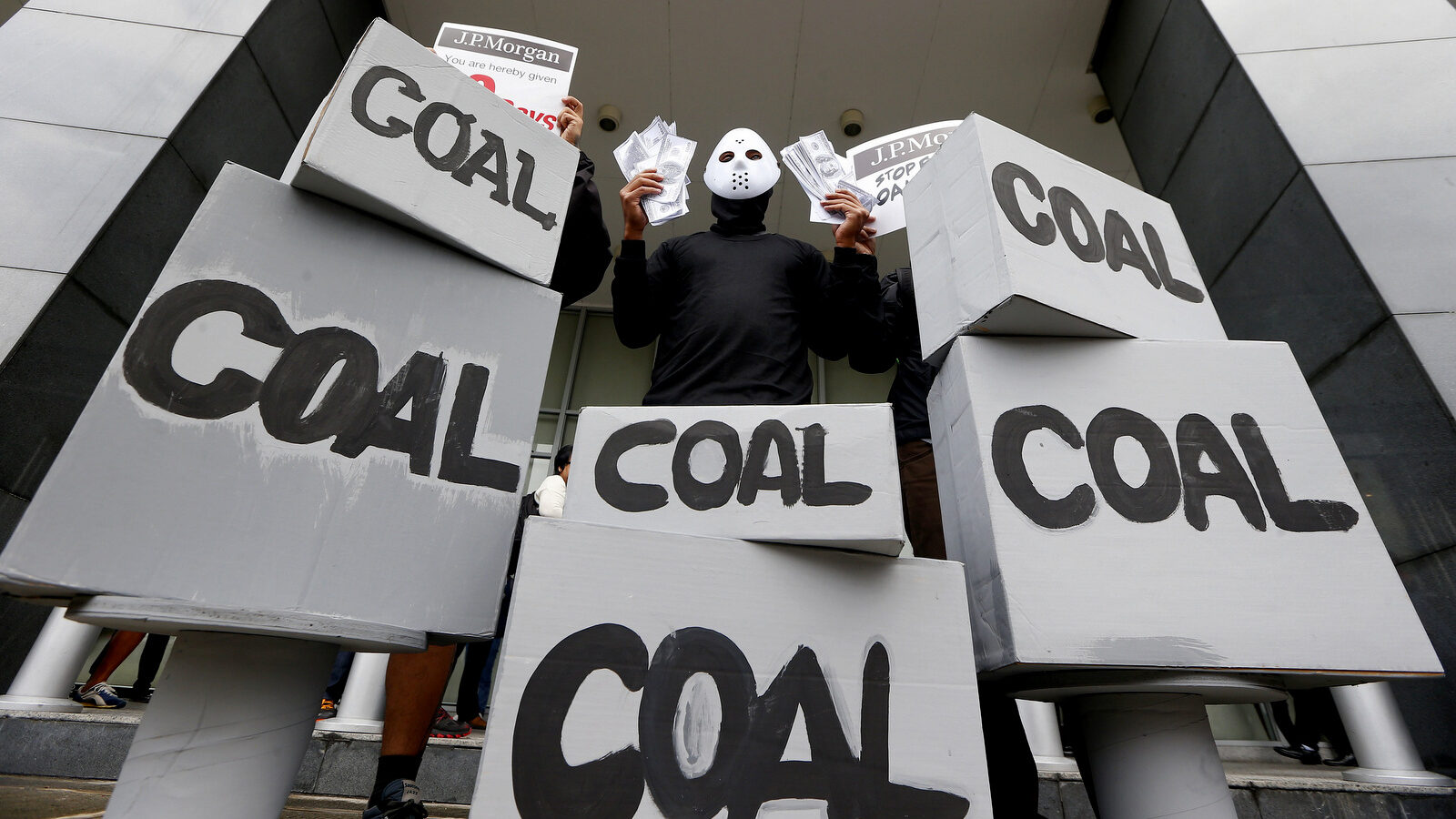 A masked environmental activist wags mock dollars bills during a protest outside the JP Morgan Chase & Co. office to urge the multi-national company to stop its funding of a coal-fired power plant in the country and other coal projects all over the world Friday, Oct. 13, 2017, in suburban Taguig city east of Manila, Philippines. (AP/Bullit Marquez)