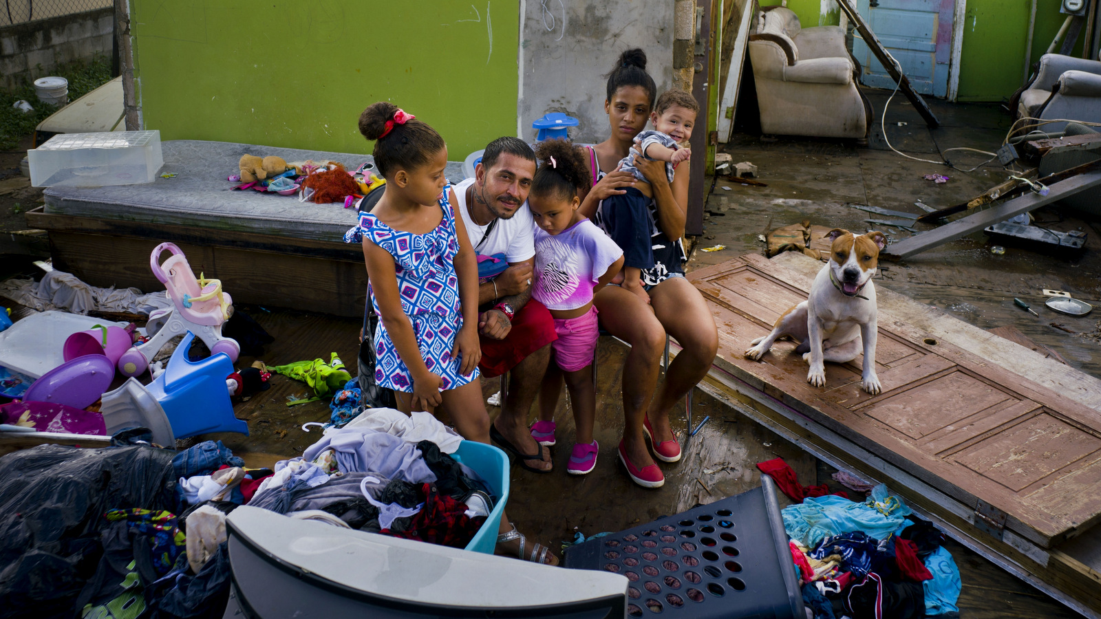 In this Saturday, Oct. 14, 2017 photo, Arden Dragoni, second from left, poses with his wife Sindy, their three children and dog Max, surrounded by what remains of their home destroyed by Hurricane Maria in Toa Baja, Puerto Rico. The Dragoni family has been living in a shelter set up at a school since the storm destroyed their wooden home in late September. They lost everything: clothes, household goods, and an old car. Dragoni supported his family by working construction, but his employers are currently out of business, leaving him and his family without a source of income. (AP/Ramon Espinosa)