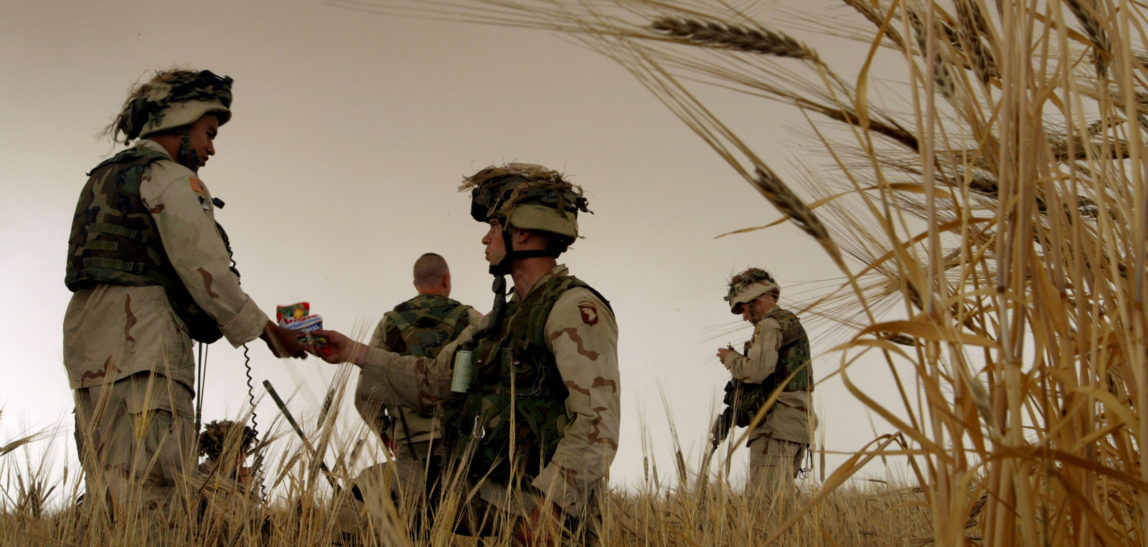 A U.S. Army soldier shares a bag of sunflower seeds with a fellow soldier, as they wait for a helicopter to pick them up in a field of barley nearly ready to harvest, outside Tall Ash Shawr, a village in northwestern Iraq, Monday, May 19, 2003. (AP/Brennan Linsley)