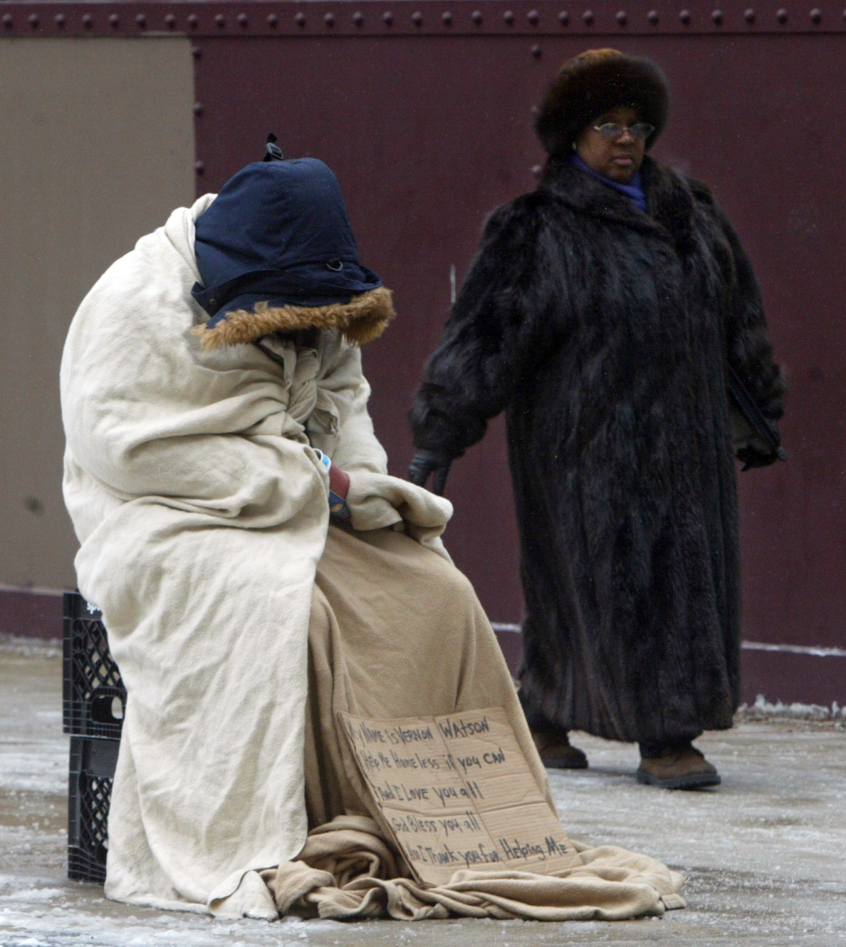 Vernon Watson, a homeless person, wraps himself in blankets as a lone pedestrian walks by on a cold Chicago street. (AP/Charles Rex Arbogast)