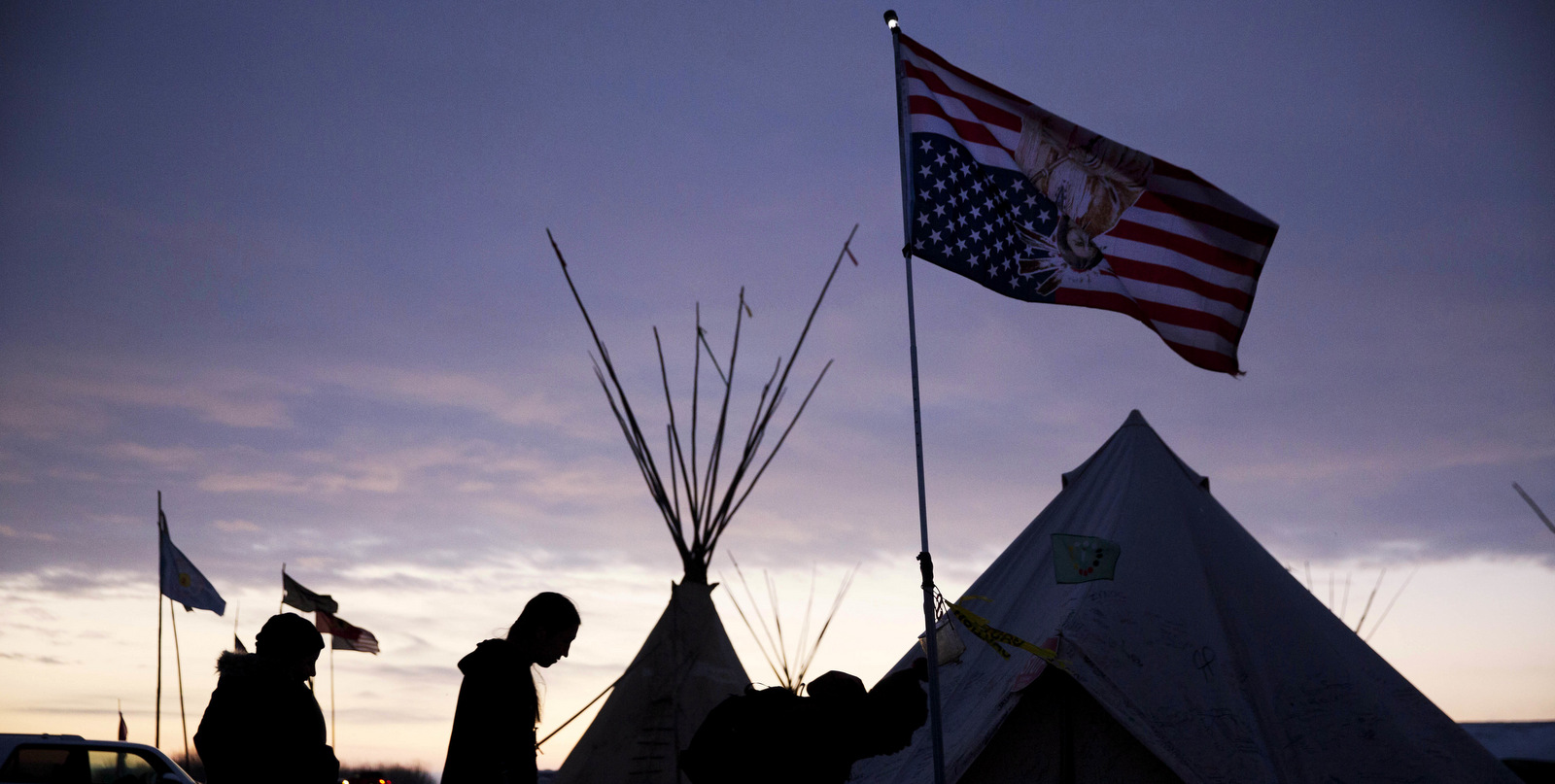 Travelers arrive at the Oceti Sakowin camp where people have gathered to protest the Dakota Access oil pipeline as they walk into a tent next to an upside-down american flag in Cannon Ball, N.D., Dec. 2, 2016. (AP/David Goldman)