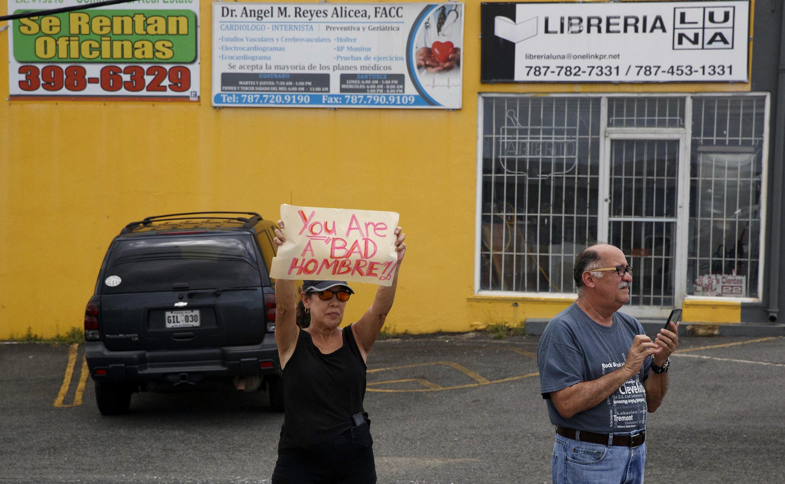 A woman holds up a protest sign as the motorcade carrying President Donald Trump passes to tour a neighborhood impacted by Hurricane Maria in Guaynabo, Puerto Rico, Oct. 3, 2017. Outside of official events, many Puerto Ricans said they won't be welcoming President Donald Trump with open arms during his visit to the storm-wracked island. (AP/Evan Vucci)