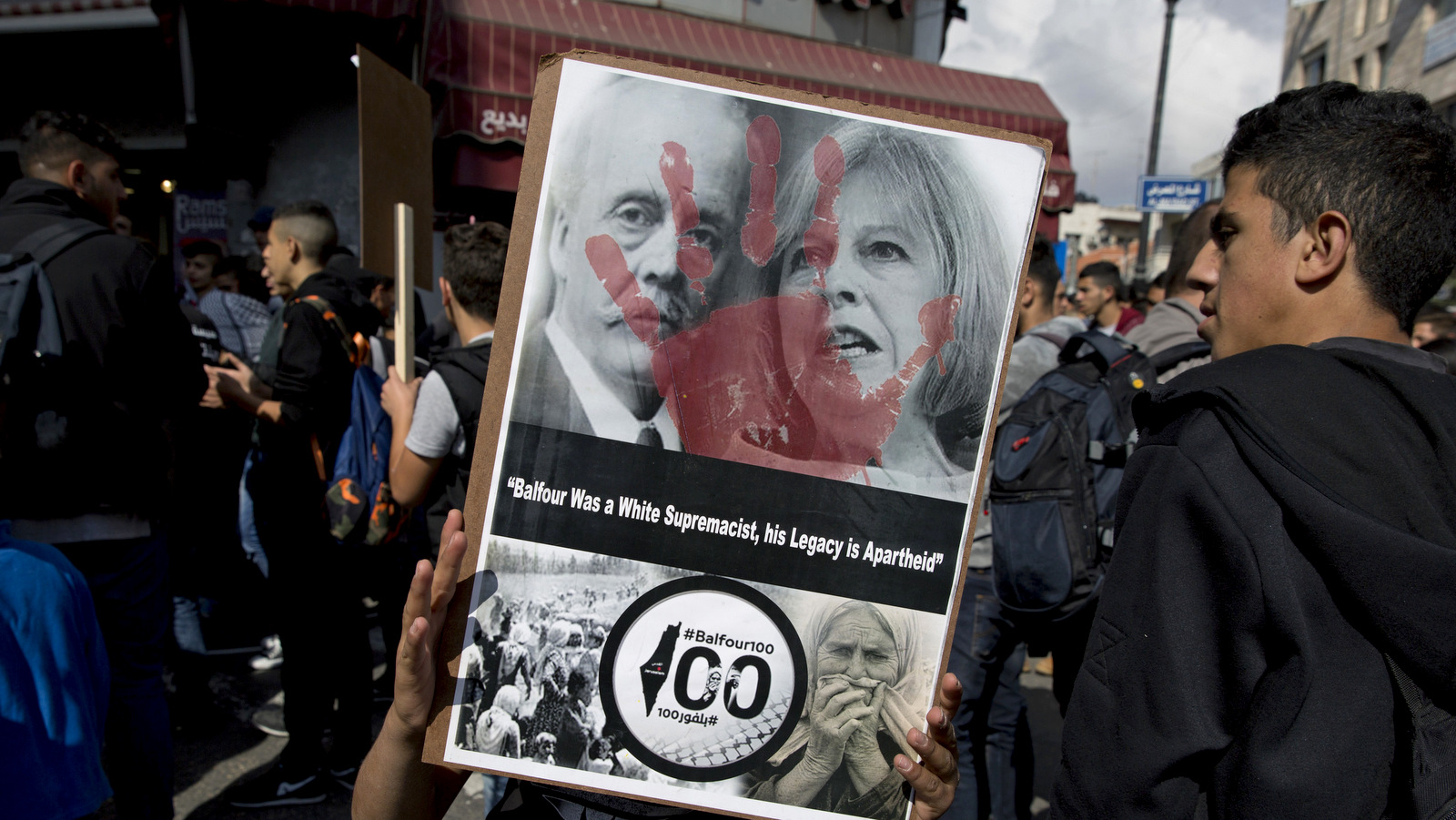 A Palestinian protester carries a poster with a defaced photo of UK Prime Minister Theresa May, and Arthur Balfour, on the 100th anniversary of the Balfour Declaration, in Ramallah, Thursday, Nov. 2, 2017. Thousands of Palestinians have taken to the streets in protest across the West Bank marking a century since the Balfour Declaration, Britain's promise to Zionists to create a Jewish home in what is now Israel. (AP Photo/Nasser Nasser)