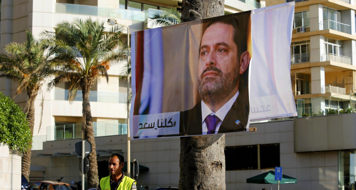 A worker stands in front of a poster of outgoing Prime Minister Saad Hariri with Arabic words that read, "We are all Saad,", in Beirut, Lebanon, Nov. 11, 2017. Lebanon's president has called on Saudi Arabia to clarify the reasons why the country's prime minister has not returned home since his resignation which was announced from the kingdom. (AP/Hassan Ammar)