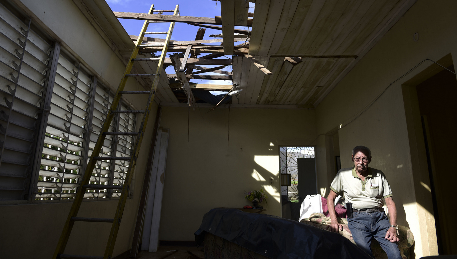 Edgardo de León sits in his living room with a hole in the ceiling caused by the whip of hurricane Maria, in Cataño, Puerto Rico. A newly created Florida company with an unproven record won more than $30 million in contracts from the Federal Emergency Management Agency to provide emergency tarps and plastic sheeting for repairs to hurricane victims in Puerto Rico. Bronze Star LLC never delivered those urgently needed supplies, which even months later remain in demand on the island, Nov. 15, 2017. (AP/Carlos Giusti)