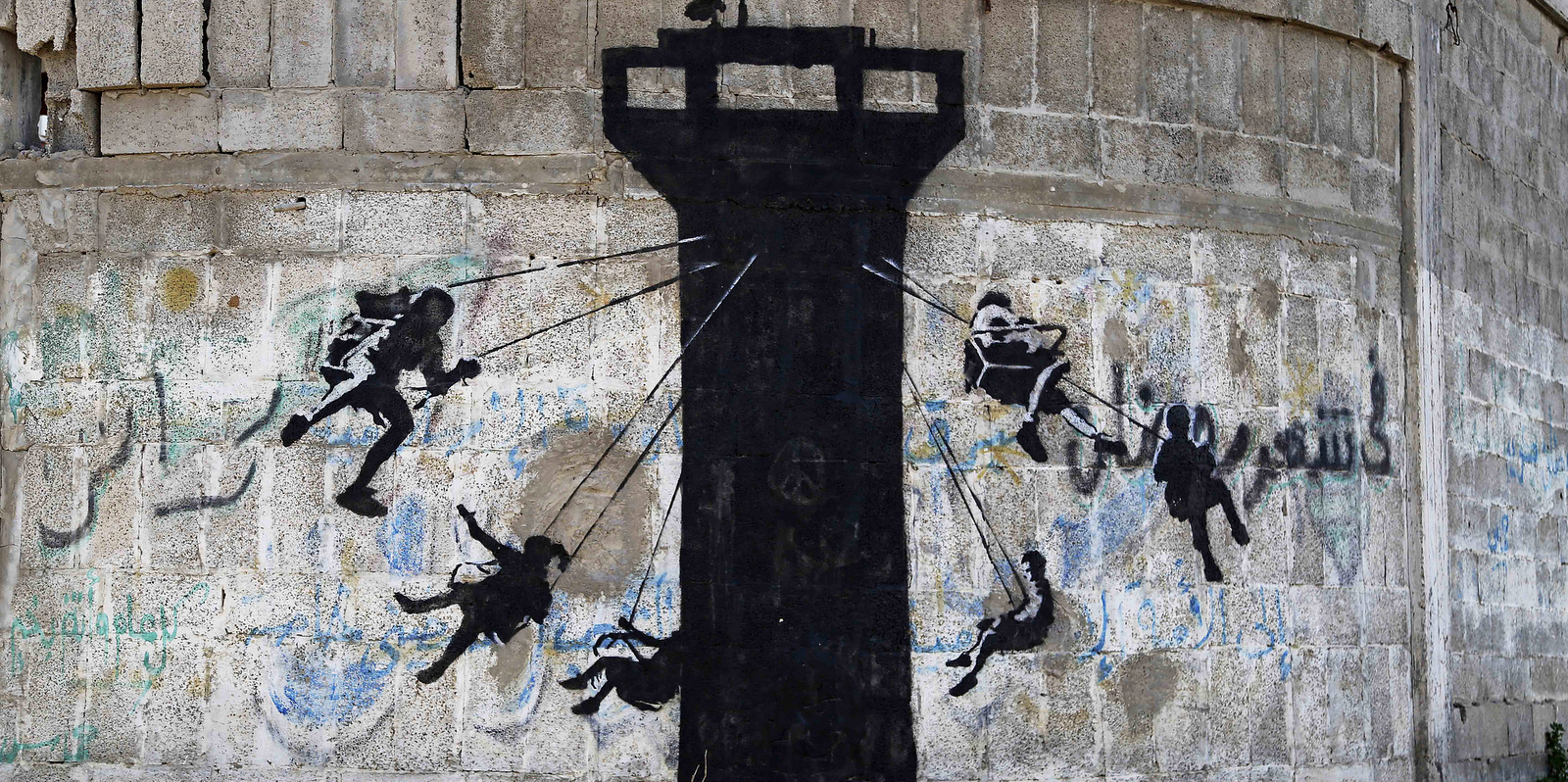 A mural of children using an Israeli army watch tower as a swing ride, presumably painted by British street graffiti artist Banksy, is seen on a wall at main wall at the main road in Beit Lahiya, in the northern Gaza Strip, Friday, Feb. 27, 2015. (AP/Adel Hana)