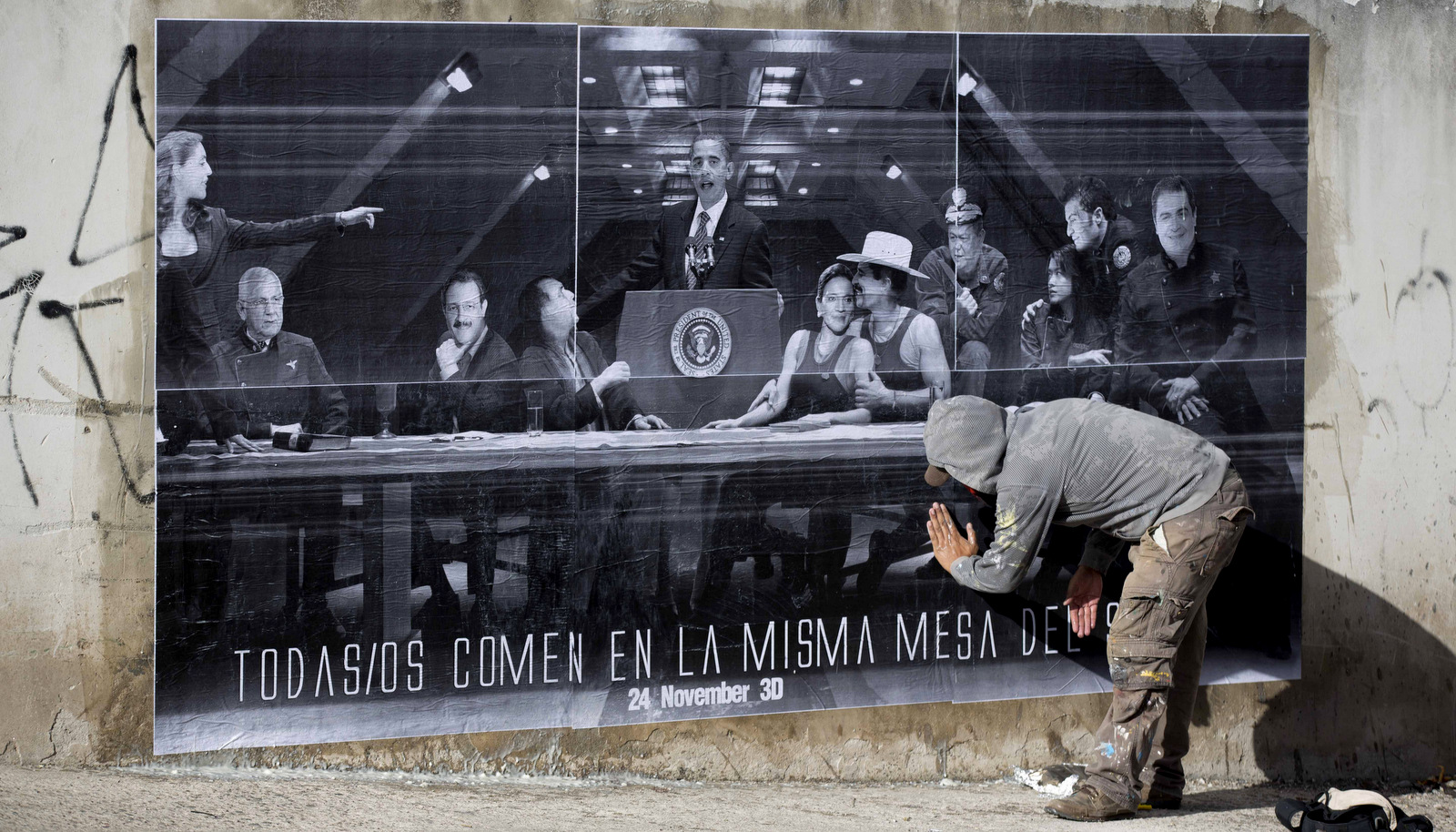 An artist who calls himself the Urban Maeztro who prefers to remain anonymous for security reasons pastes up one of his "interventions" that shows President Barack Obama at a podium surrounded by Honduran politicians and reads in Spanish "All eat at the same table as God" on a street wall days before elections in Tegucigalpa, Honduras, Nov. 21, 2013. (AP/Eduardo Verdugo)