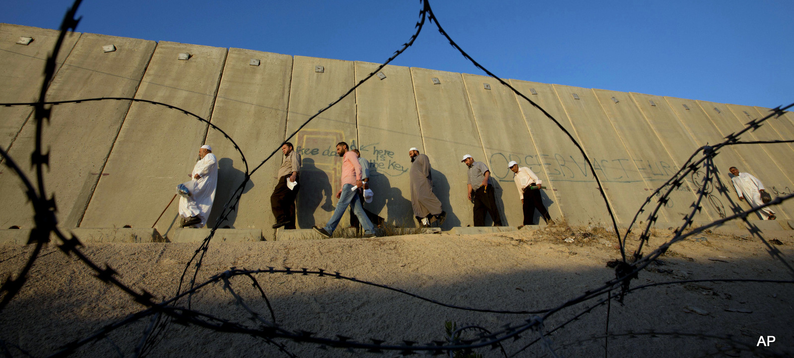 Palestinian men walk past a section of Israel's apartheid wall to cross the a checkpoint on their way to pray at the Al-Aqsa Mosque in Jerusalem, on the fourth Friday of Ramadan, at the Qalandia checkpoint between the West Bank city of Ramallah and Jerusalem, July 10, 2015. (AP/Majdi Mohammed)