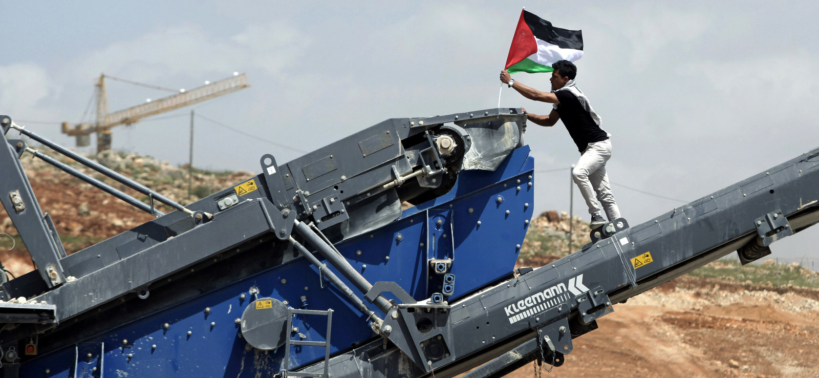 A protester posts a Palestinian flag on Israeli construction equipment at a building site adjacent to the Israeli settlement of Beitar Illit during a protest marking Land Day, in the village of Wadi Fukin, near the West Bank city of Bethlehem, March 30, 2015. (AP/Mahmoud Illean)