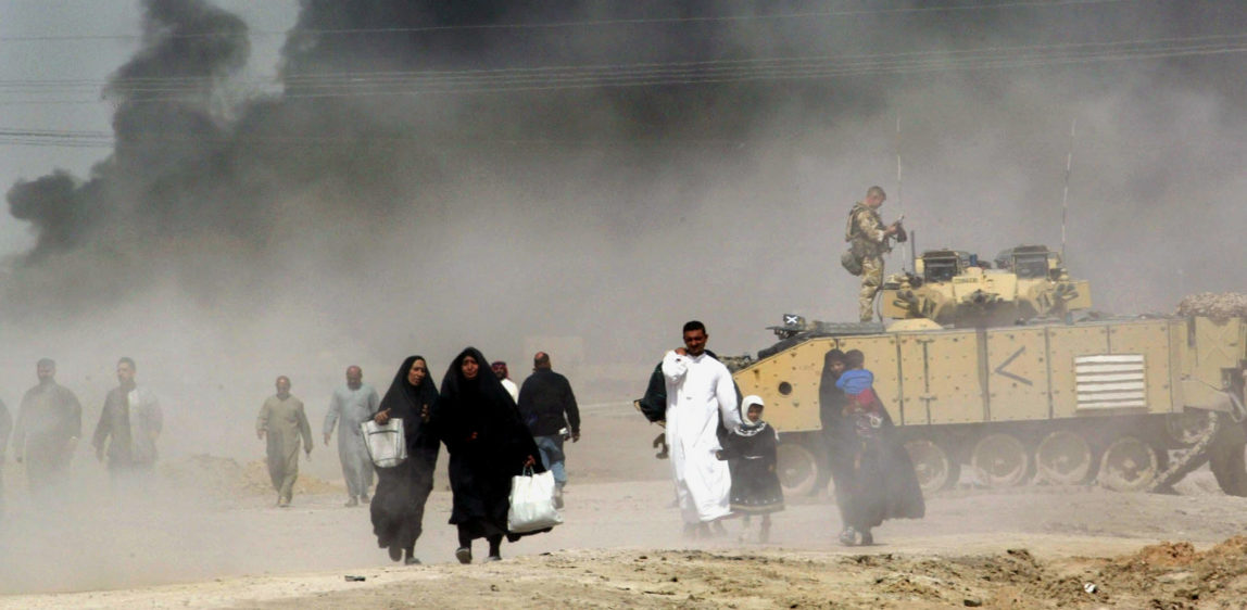 Iraqis pass by a British tank as they flee Basra, southern Iraq, as smoke looming over the city can be seen in the distance, March 29, 2003. (AP/Anja Niedringhaus)