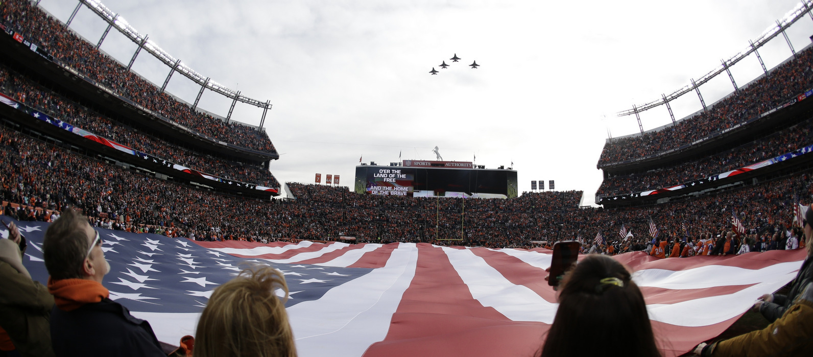 A giant U.S. flag is displayed during a military fly-over at Sports Authority Field at Mile High before an NFL football game between the Denver Broncos and the Oakland Raiders, Sunday, Jan. 1, 2017, in Denver. (AP/Jack Dempsey)