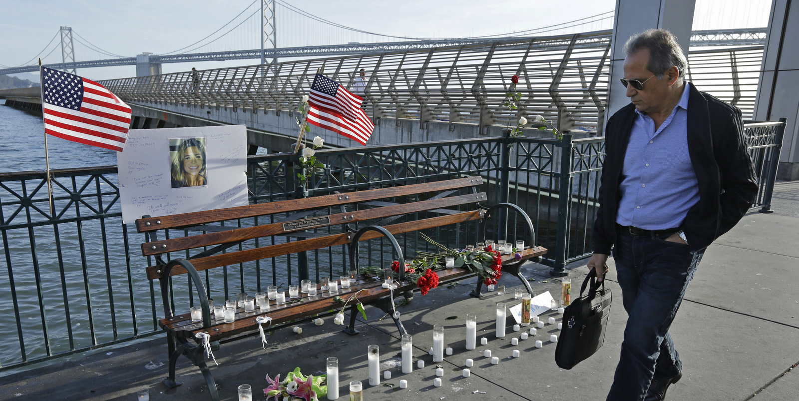 A man walks past candles, flowers, and a photo of Kate Steinle at a memorial site on Pier 14 Friday, Dec. 1, 2017, in San Francisco. In this fiercely liberal city, city leaders remained attached to San Francisco's sanctuary city status despite a not guilty verdict in a killing that sparked feverish immigration debates because the man who fired the gun was in the country illegally after being deported five times. (AP Photo/Ben Margot)