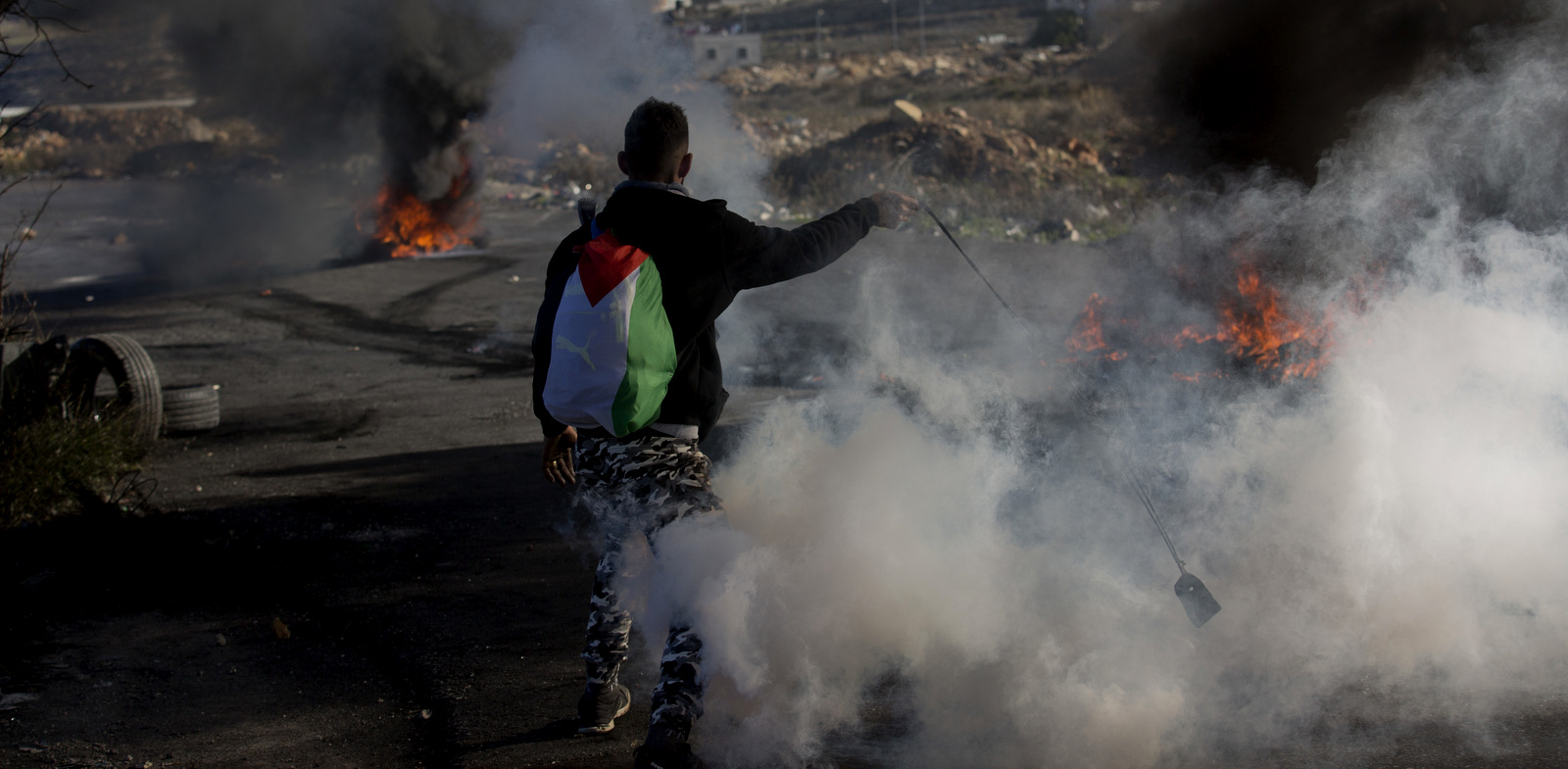 A Palestinian protester uses a slingshot amid teargas and smoke, during clashes with Israeli troops following protests against U.S. President Donald Trump's decision to recognize Jerusalem as the capital of Israel, in the West Bank city of Ramallah, Friday, Dec. 8, 2017. (AP Photo/Nasser Nasser)