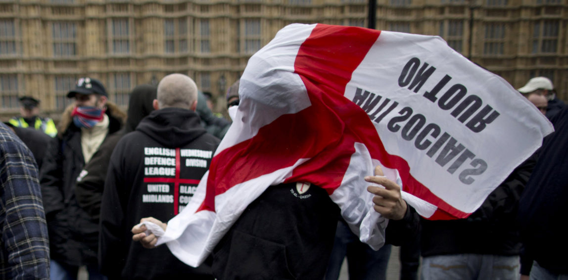 Unidentified members of the extreme far right group the English Defense League as a English flag is blown over his face, during a protest outside the Houses of Parliament in London, Oct. 27, 2012. (AP/Matt Dunham)