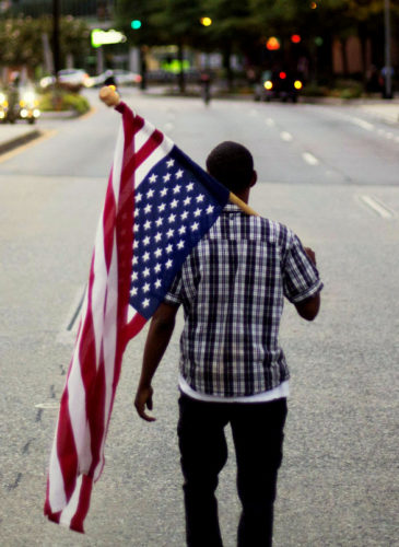 Skylar Barrett walks alone with an American flag in the middle of the street during a march through the Buckhead neighborhood against the recent police shootings of African-Americans on July 11, 2016, in Atlanta. (AP/David Goldman)