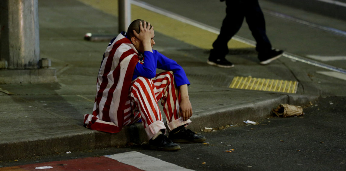 A man dressed in red-white-and-blue sits on the curb during a protest against President-elect Donald Trump, Wednesday, Nov. 9, 2016, in Seattle's Capitol Hill neighborhood. (AP Photo/Ted S. Warren)