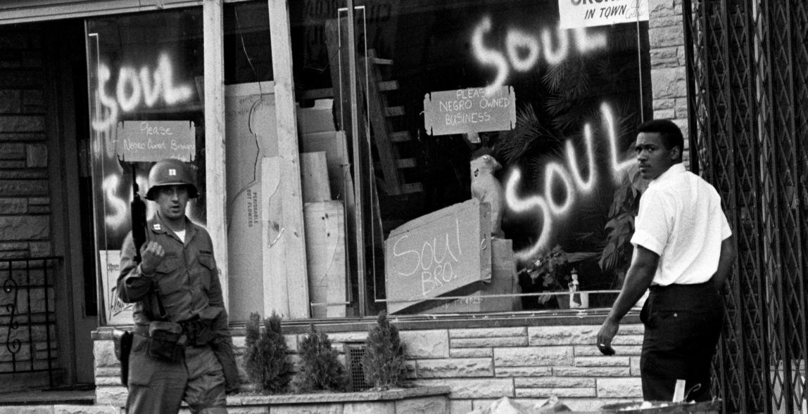 In this July 15, 1967, file photo, a National Guard officer passes the smashed window of a black-owned flower shop in riot-torn Newark, N.J. (AP Photo)