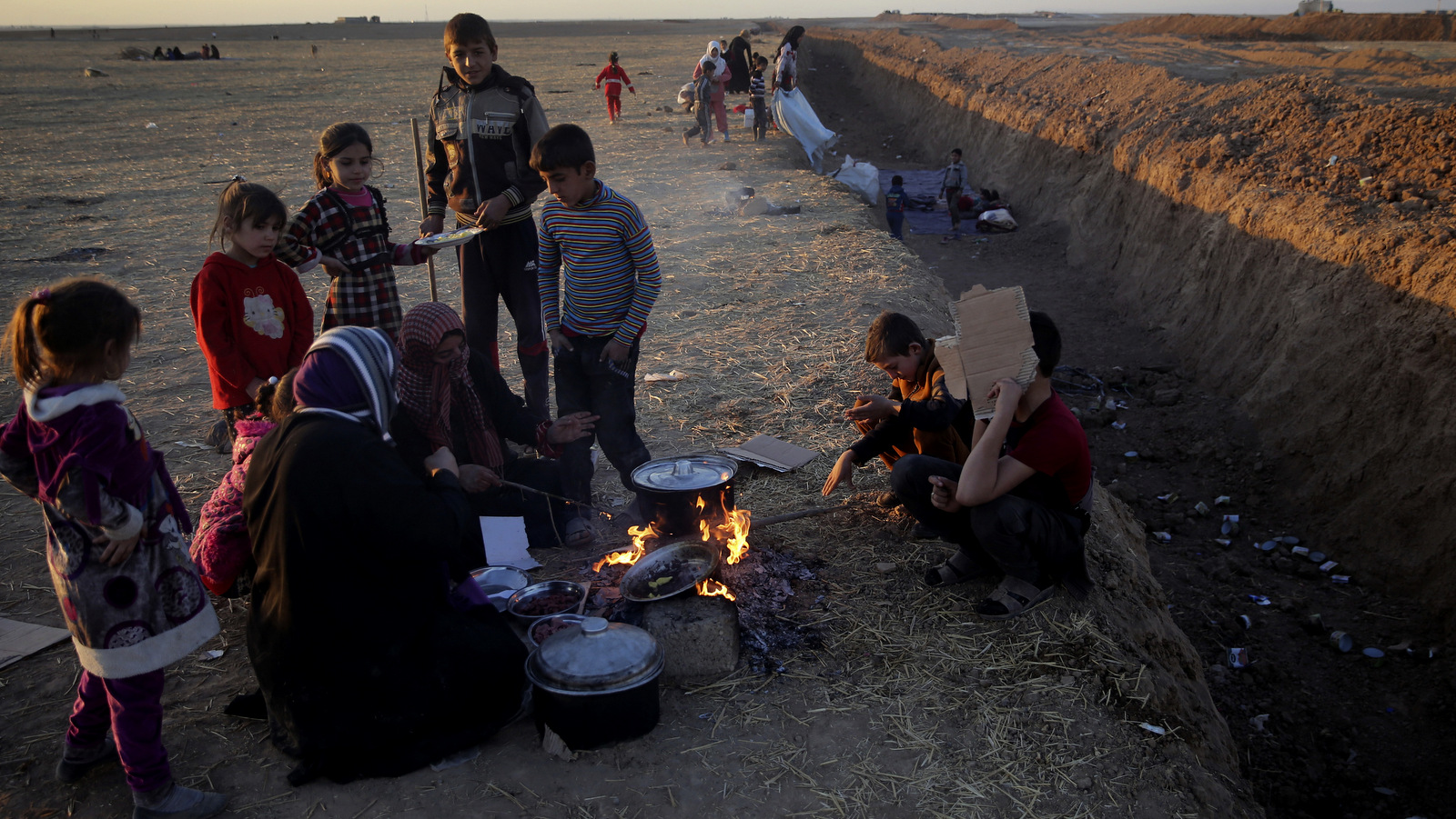 Las familias que huyeron de ISIS cocinan junto a una trinchera creada por las fuerzas kurdas para demarcar su frontera, mientras esperan cruzar a las áreas kurdas, en la llanura de Nínive, al noreste de Mosul. Las bermas de arena y las trincheras serpentean a lo largo del norte de Irak hasta Siria, junto a carreteras recién pavimentadas y extensos puestos de control adornados con banderas kurdas, en lo que cada vez más se parece a una frontera internacional. (AP / Hussein Malla)