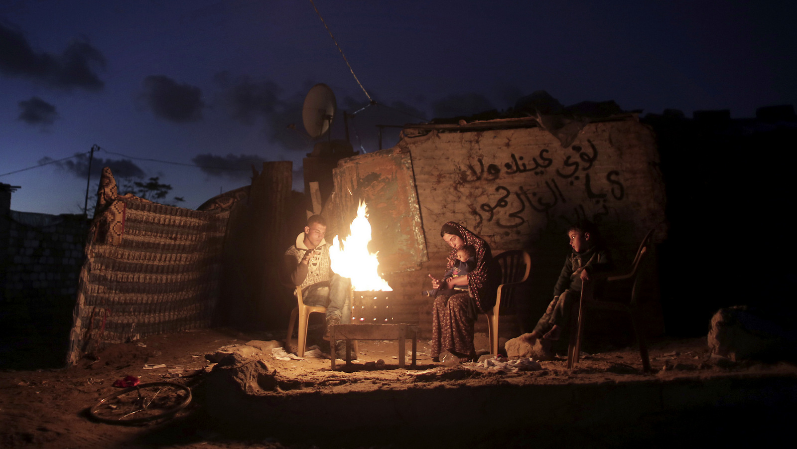 A Palestinian family warm themselves on a fire outside their makeshift home during a power cut in Khan Younis in the southern Gaza Strip. (AP/ Khalil Hamra)