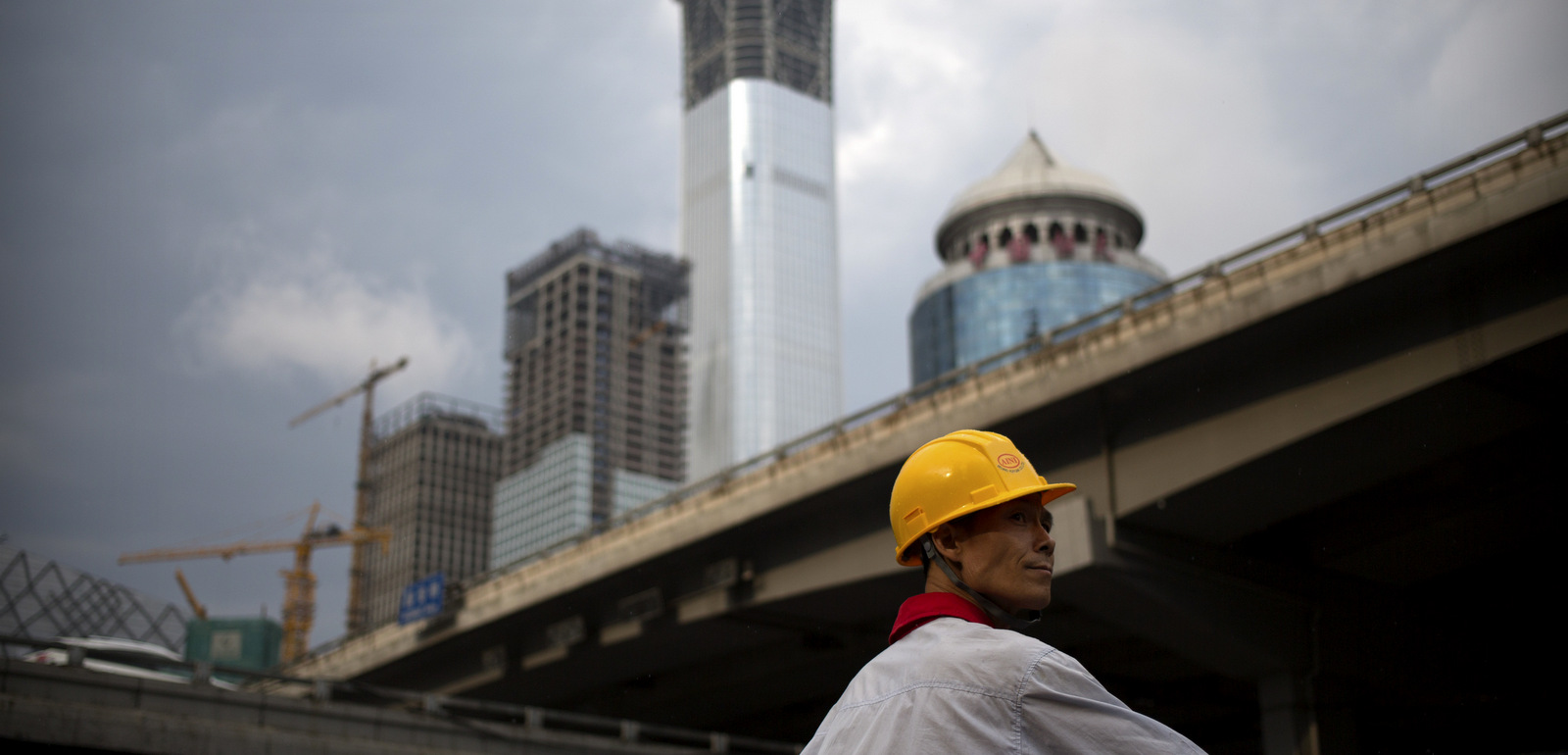 A construction worker waits to cross an intersection near buildings under construction in the central business district of Beijing, Aug. 16, 2017.  (AP/Mark Schiefelbein)