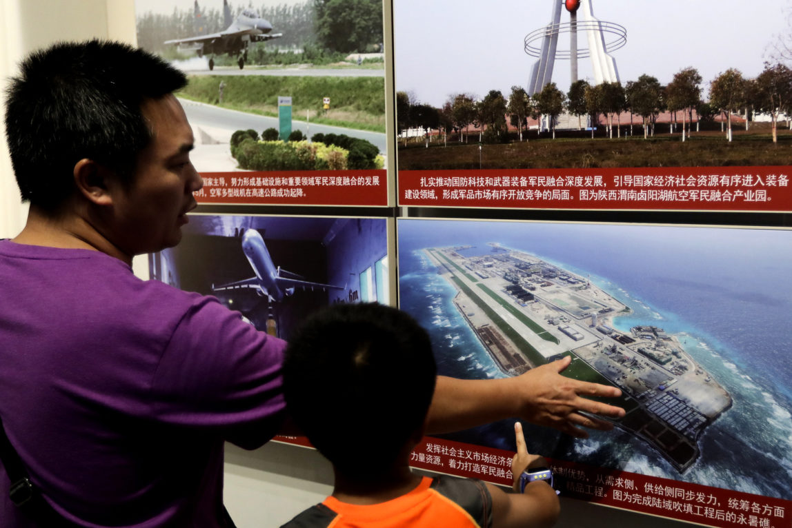 A man and a child look at a picture showing the Fiery Cross Reef in the Spratly islands, in the disputed South China Sea, on display at the military museum in Beijing, July 27, 2017. (AP/Andy Wong)