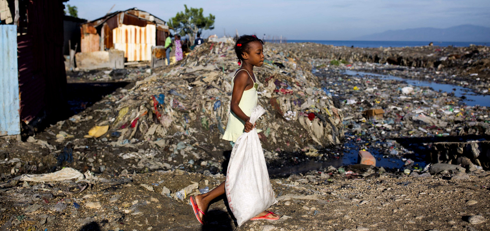 A girl takes out the trash to an open air dump, behind, in the Cite Soleil slum of Port-au-Prince, Haiti, Nov. 21, 2017. (AP/Dieu Nalio Chery)
