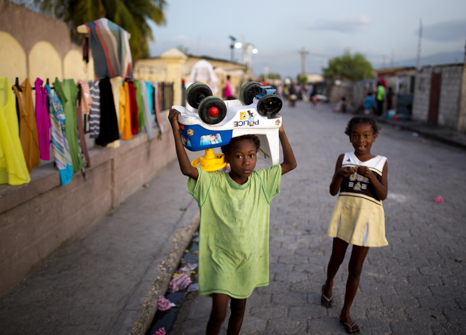 A girl carries her toy police car home along with her sister in the Cite Soleil slum of Port-au-Prince, Haiti, Dec. 27, 2017. (AP/Dieu Nalio Chery)