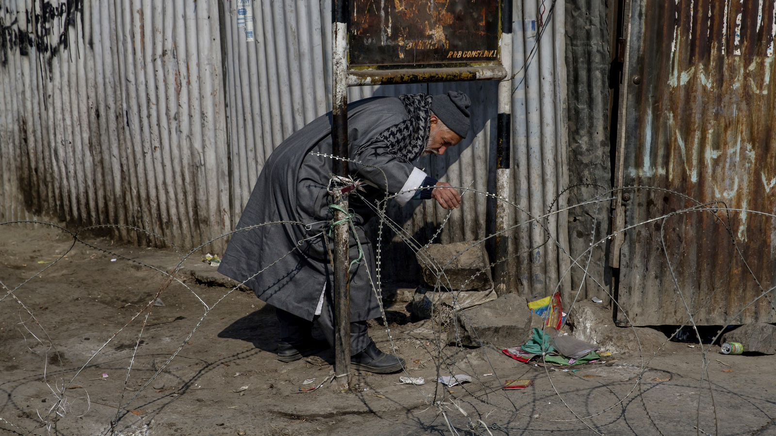 An elderly Kashmiri man kneels to walk under an iron hoarding as he makes his way past a barbed-wire road checkpoint set up by Indian security forces during a curfew in Srinagar, Indian occupied Kashmir, Feb. 9, 2017. (AP/Dar Yasin)