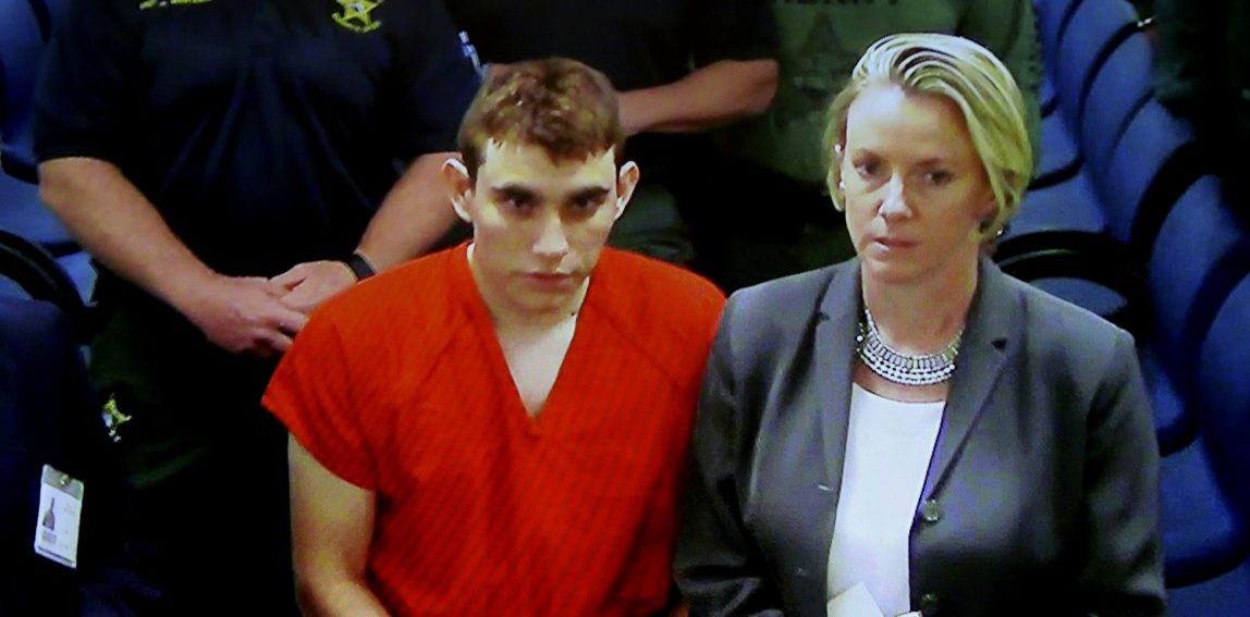 A video monitor shows school shooting suspect Nikolas Cruz, left, making an appearance before Judge Kim Theresa Mollica in Broward County Court, Thursday, Feb. 15, 2018, in Fort Lauderdale, Fla. Cruz is accused of opening fire Wednesday at the school killing more than a dozen people and injuring several. (Susan Stocker/South Florida Sun-Sentinel via AP)