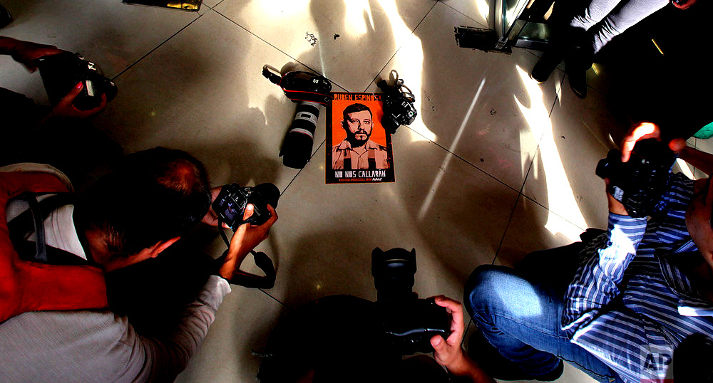 Journalists gather around a photo of slain photojournalist Ruben Espinosa, placed by his relatives at the entrance of Mexico City's Attorney General's office, on the second year anniversary of his murder in Mexico City, Monday, July 31, 2017. Espinosa worked for the investigative magazine Proceso and other media in the Mexican state of Veracruz, and murdered along with four women in an apartment in Mexico City on July 31, 2015. (AP Photo/Marco Ugarte)