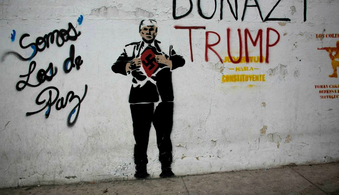 A mural of U.S. President Donald Trump depicting him wearing a Nazi swastika covers a wall along a sidewalk in Caracas, Venezuela, Nov. 14, 2017, along with the Spanish message: "We are those of peace.” (AP/Ariana Cubillos)