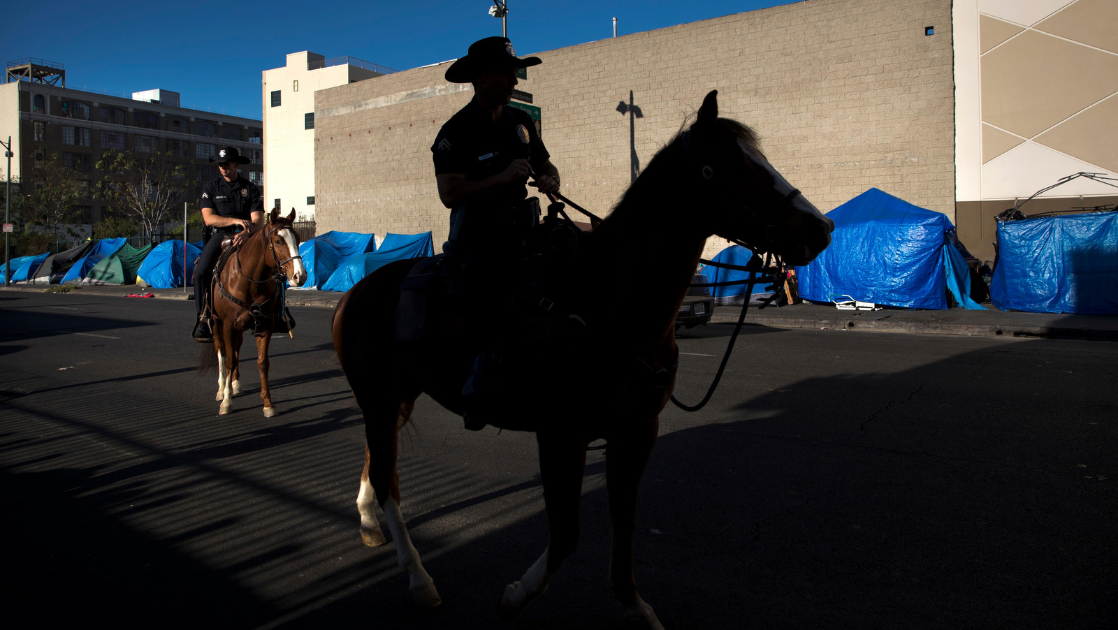 Tents belonging to homeless people are covered with tarps as Los Angeles police officers on horses patrol in the Skid Row area of downtown Los Angeles Friday, Dec. 1, 2017. A homeless crisis of unprecedented proportions is rocking the West Coast, and its victims are being left behind by the very things that mark the region's success: soaring housing costs, rock-bottom vacancy rates and a roaring economy that waits for no one. (AP/Jae C. Hong)